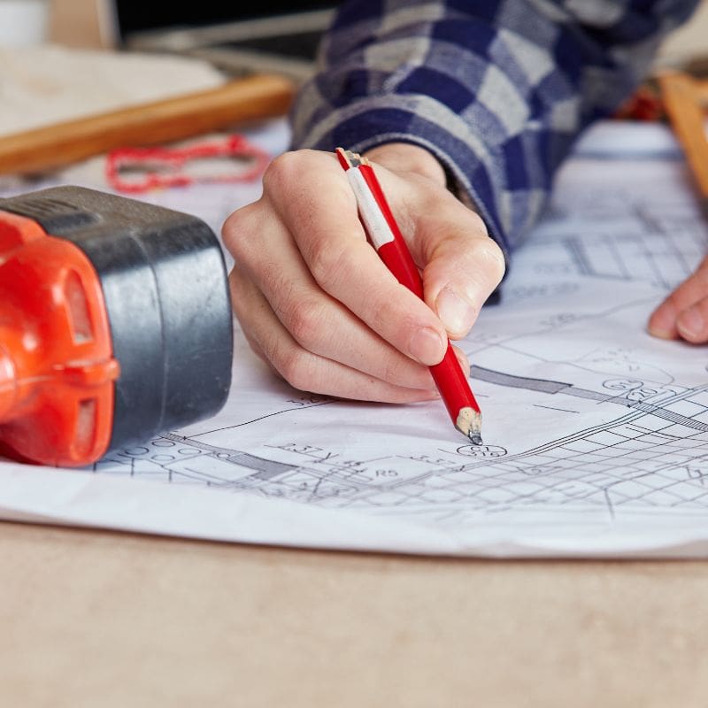 man making a note on a floor plan with a drill laying on the table next to him