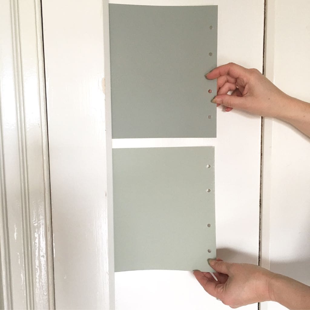 Person holding two paint samples of a light and dark green against a white wall.