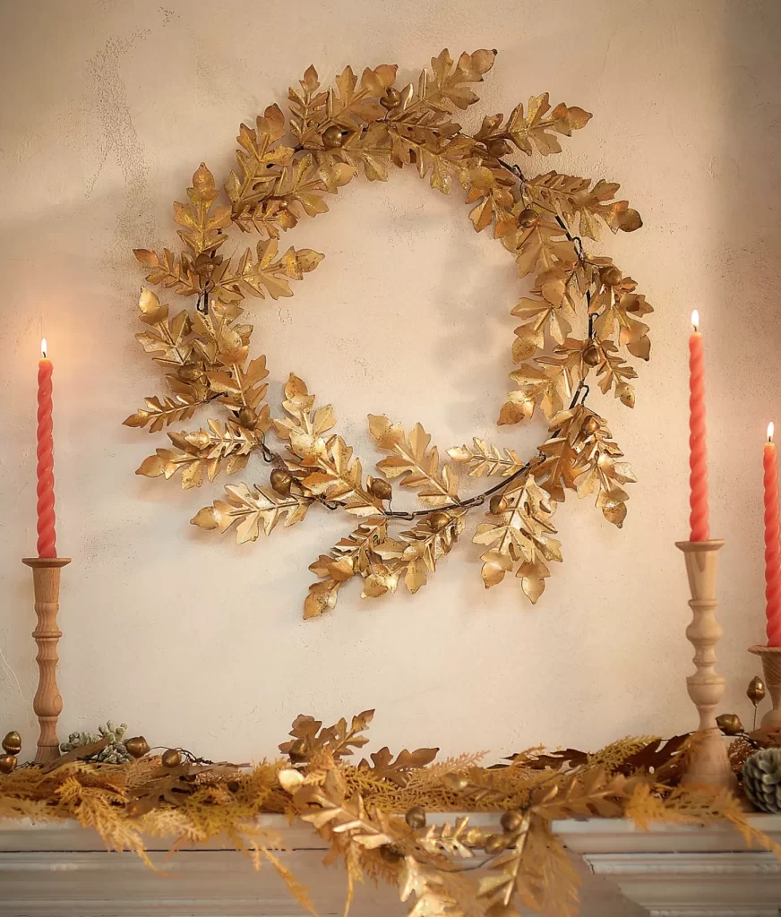 Gilded Acorn + Oak Leaf Wreath from Anthropologie above a mantle with gold garland and candles.