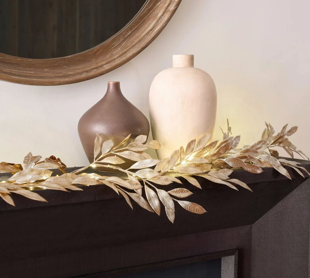 Leafy Glam String Lights Garland from Anthropologie on a dark wood mantle next to a taupe and white vase