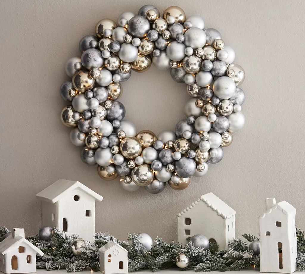 Lit Ornament Frosted Pine Wreath & Garland from Pottery Barn on a taupe wall over miniature ceramic houses