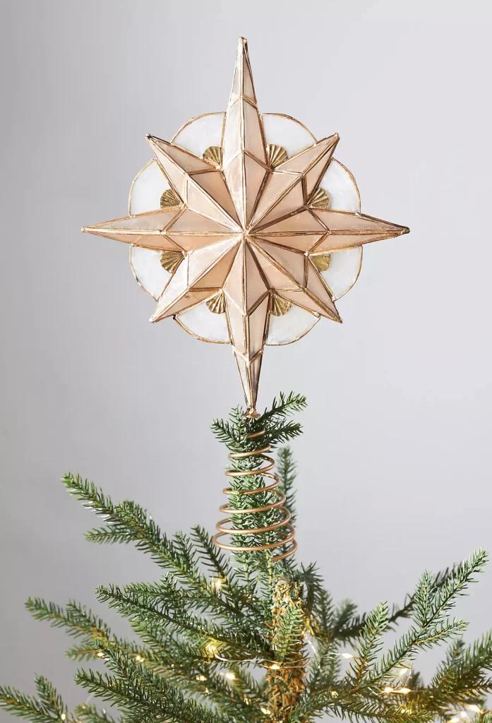 Star Tree Topper from Anthropologie on top of a Christmas tree on a white background