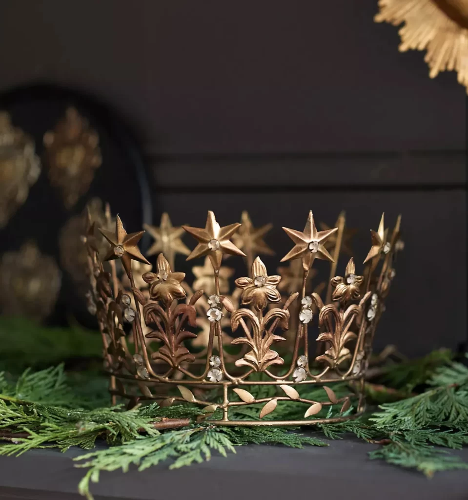 Starry Crown in gold from Anthropologie sitting on holly branches on a dark gray background