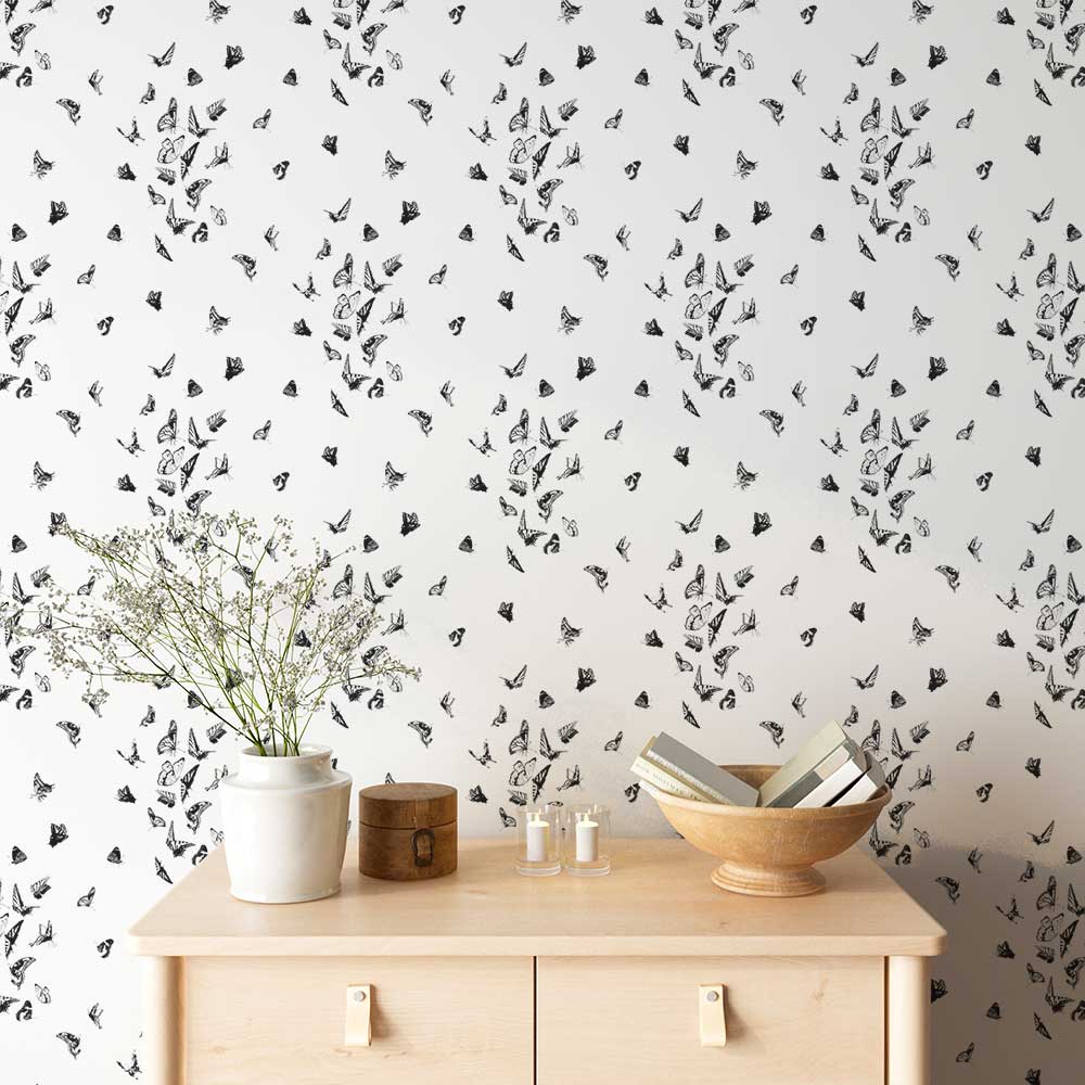 Butterfly Dance Wallpaper in Noir behind a light wood console with a vase and bowl.